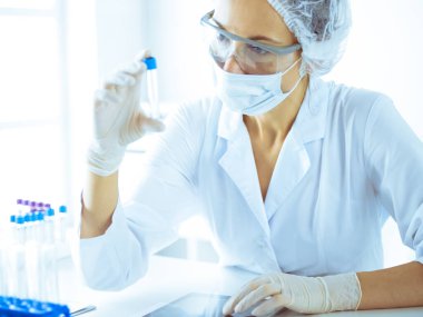 Koruyucu gözlüklü profesyonel kadın bilim adamı labaratuvarda mavi renkte reaksiyonlarla araştırma tüpü kullanıyor. Tıp ve bilim araştırmaları kavramları