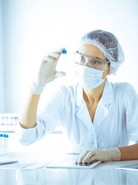 Koruyucu gözlüklü profesyonel kadın bilim adamı labaratuvarda mavi renkte reaksiyonlarla araştırma tüpü kullanıyor. Tıp ve bilim araştırmaları kavramları