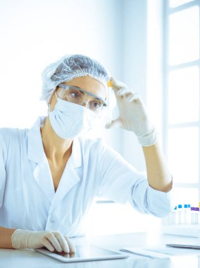 Koruyucu gözlüklü profesyonel kadın bilim adamı labaratuvarda mavi renkte reaksiyonlarla araştırma tüpü kullanıyor. Tıp ve bilim araştırmaları kavramları