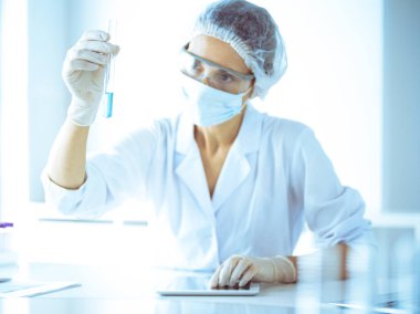 Koruyucu gözlüklü profesyonel kadın bilim adamı labaratuvarda mavi renkte reaksiyonlarla araştırma tüpü kullanıyor. Tıp ve bilim araştırmaları kavramları