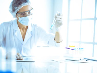 Koruyucu gözlüklü profesyonel kadın bilim adamı labaratuvarda mavi renkte reaksiyonlarla araştırma tüpü kullanıyor. Tıp ve bilim araştırmaları kavramları