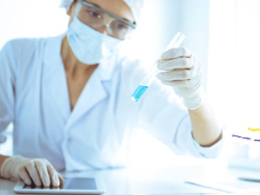 Koruyucu gözlüklü profesyonel kadın bilim adamı laboratuarda reaktörlerle araştırma tüpü kullanıyor. Tıp ve araştırma kavramları