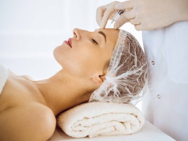 Güzel bir kadın tıp merkezinde kapalı gözlerle güzellik iğneleri yaptırıyor. Güzellik uzmanı elleri şırıngayla kadın yüzüne güzellik prosedürü uyguluyor. Kozmetik tıp ve cerrahi konsepti