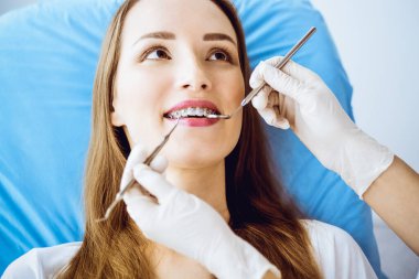 Diş hekiminde dişçi tarafından muayene edilen diş telleriyle gülümseyen genç bir kadın. Sağlıklı dişler ve tıbbi bakım konsepti