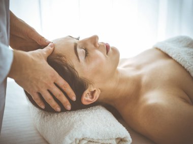 Güzel esmer kadın yüz masajından zevk alıyor. Gözleri kapalı ve mutlu. Tıp ve kaplıca merkezi kavramlarında rahatlatıcı tedavi