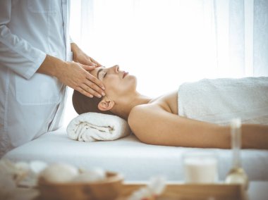 Güzel esmer kadın yüz masajından zevk alıyor. Gözleri kapalı ve mutlu. Tıp ve kaplıca merkezi kavramlarında rahatlatıcı tedavi