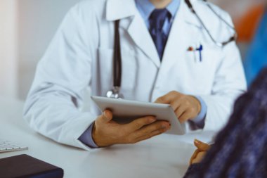 Dost canlısı erkek doktor ve hasta kadın güneşli klinikte otururken sağlık muayenesini tartışıyorlar.