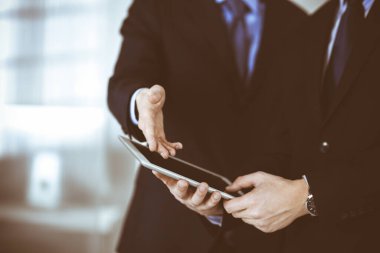 İş adamları yeni projelerini tartışmak için bir tablet bilgisayar kullanıyorlar, modern bir ofiste duruyorlar. İş yerinde iş arkadaşı olan tanınmamış bir iş adamı ya da erkek girişimci. Takım çalışması ve ortaklık