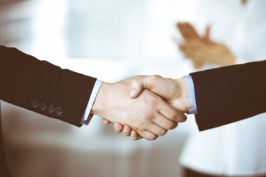 İş adamları toplantıda ya da pazarlıkta el sıkışıyor, yakın plan. Bir grup tanınmamış iş adamı ve modern bir ofiste duran bir kadın. Takım çalışması, ortaklık ve el sıkışma kavramı