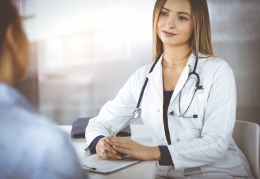 Genç zeki kadın-doktor, bir klinikteki güneşli dolapta yan yana otururken hastalarının semptomlara alerji göstermelerini dinliyor. Steteskopu olan kadın hekim,