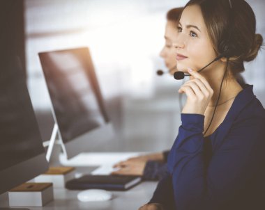 İki iş kadını, güneşli bir modern ofiste masada otururken, müşterilerle kulaklıkla sohbet ediyorlar. Çağrı merkezinde çeşitli insanlar. Tele pazarlama ve müşteri hizmetleri