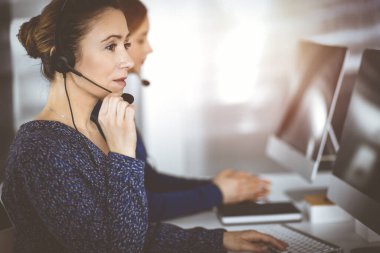 İki iş kadını, güneşli bir modern ofiste masada otururken, müşterilerle kulaklıkla sohbet ediyorlar. Çağrı merkezinde çeşitli insanlar. Tele pazarlama ve müşteri hizmetleri