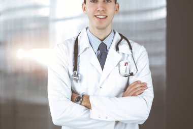 Klinikte kolları kavuşturulmuş gülümseyen adam-doktor. Hastanede genç ve zeki bir doktorla mükemmel bir tıbbi hizmet. Tıp konsepti