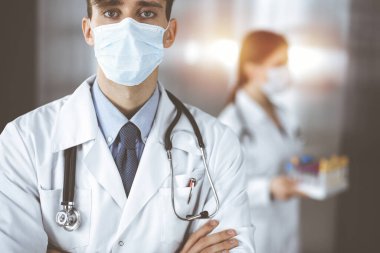 Klinikte kolları çapraz duran genç bir erkek doktor. Modern hastanede tıbbi koruyucu maske takan zeki bir doktor. Tıp ve Corona virüsü kavramı