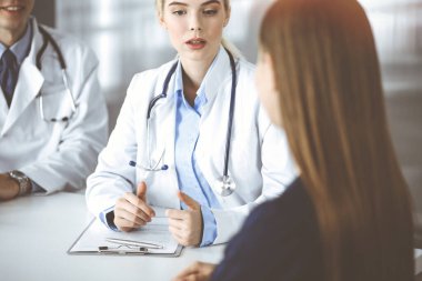 Erkek meslektaşı olan kadın-doktor, modern klinikteki masada otururken hasta kadına danışıyor. Mükemmel sağlık hizmeti, tıp konsepti