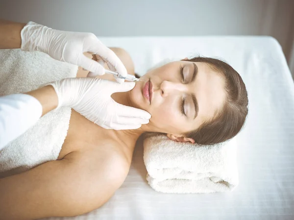 Beautician doing beauty procedure with syringe to face of young brunette woman. Cosmetic medicine and surgery, beauty injections