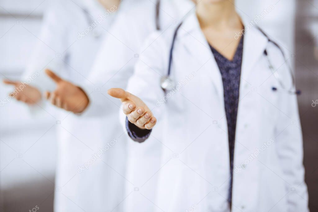 Doctors standing as a team while offering helping hand for shaking hand or saving life in clinic