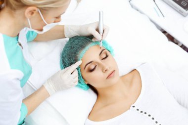 Kadın yüzüne kaş dövmesi yapan profesyonel bir güzellik uzmanı. Güzellik salonunda kalıcı kaş makyajı, yakın çekim. Kozmetoloji tedavisi