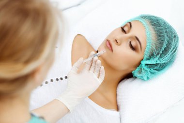 Profesyonel kozmetik uzmanı yüzüne ve dudaklarına iğne yapıyor. Genç bir kadın, yüz hatları ya da büyütme için doldurucu iğneyle doldurulur. Yaşlanma, gençleşme ve hidrasyon prosedürleriyle yüzleş