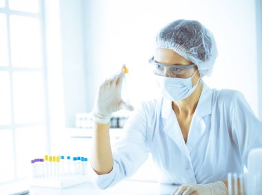 Koruyucu gözlüklü profesyonel kadın bilim adamı labaratuvarda mavi renkte reaksiyonlarla araştırma tüpü kullanıyor. Tıp ve bilim araştırmaları kavramları