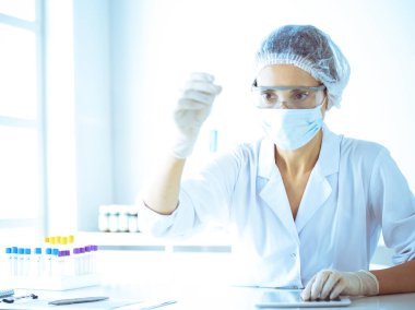 Koruyucu gözlüklü profesyonel kadın bilim adamı labaratuvarda mavi renkte reaksiyonlarla araştırma tüpü kullanıyor. Tıp ve bilim araştırmaları kavramları