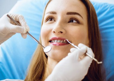 Diş hekiminde dişçi tarafından muayene edilen diş telleriyle gülümseyen genç bir kadın. Sağlıklı dişler ve tıbbi bakım konsepti