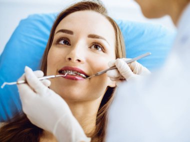 Diş hekiminde dişçi tarafından muayene edilen diş telleriyle gülümseyen genç bir kadın. Sağlıklı dişler ve tıbbi bakım konsepti