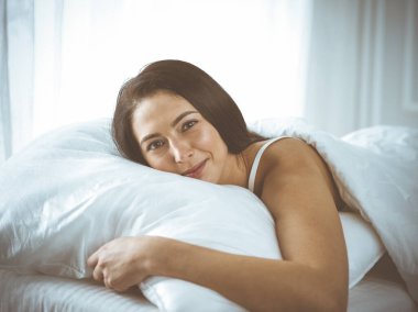 Güzel, genç, esmer kadın yatakta rahat ve mutlu bir şekilde yatarken uyuyor. Günaydın konsept.