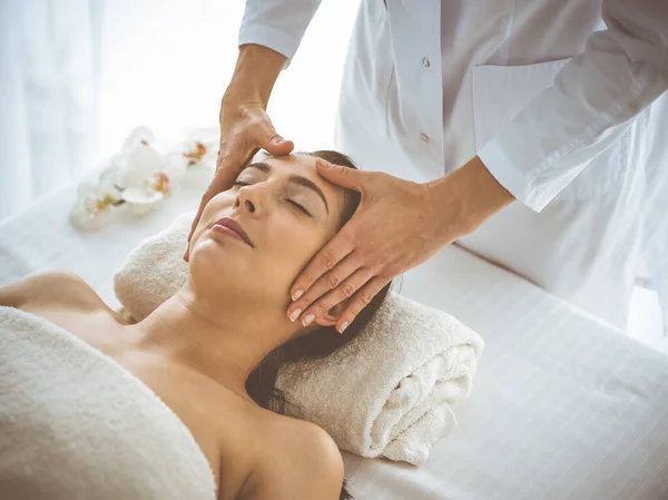 Beautiful brunette woman enjoying facial massage with closed eyes comfortable and blissful. Relaxing treatment in medicine and spa center concepts — 스톡 사진