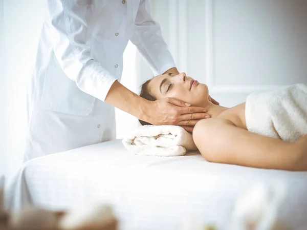 Beautiful brunette woman enjoying facial massage with closed eyes comfortable and blissful. Relaxing treatment in medicine and spa center concepts — Stock Photo, Image