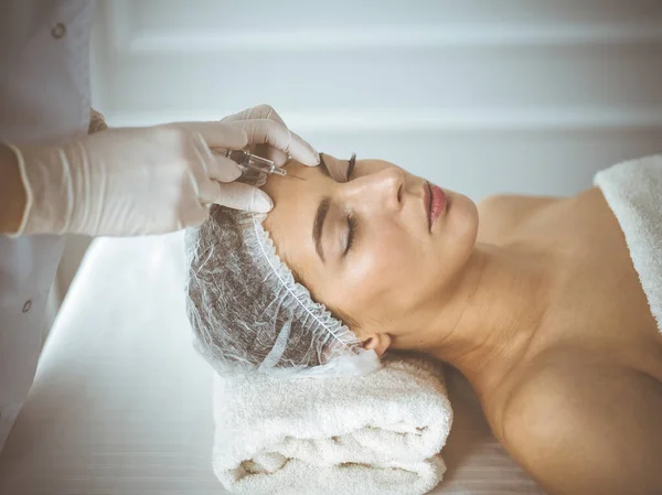 Beautician doing beauty procedure with syringe to face of young brunette woman. Cosmetic medicine and surgery, beauty injections