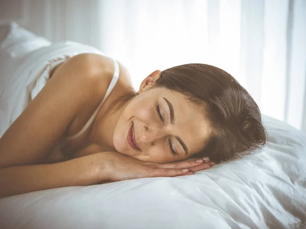 Güzel, genç, esmer kadın yatakta rahat ve mutlu bir şekilde yatarken uyuyor. Günaydın konsept. — Stok fotoğraf