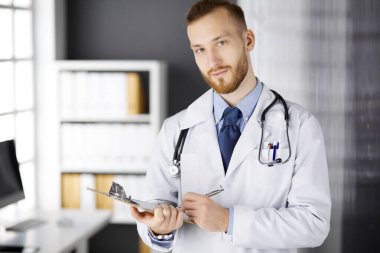 Dost canlısı kızıl sakallı doktor çalışma yerindeki klinikte panoya yazı yazıyor. Hastanede mükemmel bir tıbbi hizmet. İlaç, sağlık hizmetleri