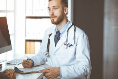 Dost canlısı kızıl sakallı doktor ve hasta kadın güneşli klinikte otururken sağlık muayenesini tartışıyorlar. İlaç, sağlık ve virüs koruma programları