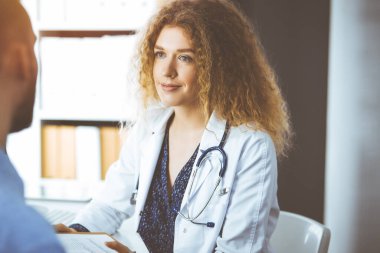 Kadın doktor ve erkek hasta güneşli klinikte otururken mevcut sağlık muayenesini tartışıyorlar.