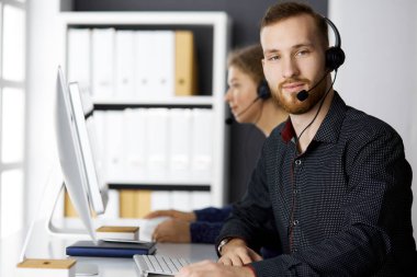 Modern ofiste otururken kulaklıkla konuşan sakallı iş adamı. Çağrı merkezinde çeşitli insanlar var. Tele pazarlama ve müşteri hizmetleri