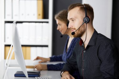 Modern ofiste otururken kulaklıkla konuşan sakallı iş adamı. Çağrı merkezinde çeşitli insanlar var. Tele pazarlama ve müşteri hizmetleri