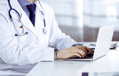 Bilinmeyen bir erkek doktor klinikte dizüstü bilgisayarla yakın planda çalışıyor. İşteki genç doktor. Mükemmel sağlık hizmeti, tıp konsepti