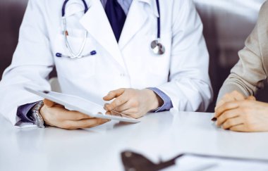 Bilinmeyen erkek doktor ve hasta kadın klinikte oturup tablet bilgisayar kullanırken bir şeyler tartışıyorlar. Hastanedeki en iyi sağlık hizmeti, ilaç, salgın durdurma.