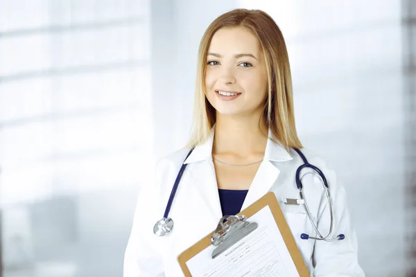 Молодая оптимистичная женщина-врач держит планшет в руках, стоя в клинике. Портрет дружелюбной женщины-врача со стетоскопом. Идеальное медицинское обслуживание в больнице. Медицина — стоковое фото