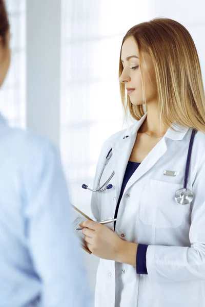 La jeune femme-médecin et sa patiente discutent de l'examen de santé actuel des patients, tout en restant ensemble dans un bureau d'hôpital. Une femme médecin écrit des marques à l'aide d'un presse-papiers. Parfait. — Photo