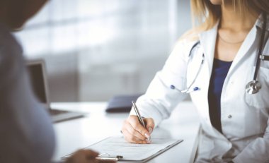 Bilinmeyen kadın doktor, bir klinikteki dolapta otururken hastasına bazı antibiyotikler yazıyor. Steteskoplu kadın doktor panoya yazı yazıyor, kapat