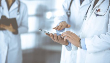 Bilinmeyen bir grup doktor hastane ofisinde dururken bazı tıbbi isim kayıtlarını kontrol etmek için bir bilgisayar tableti kullanıyor. Doktorlar hastaları muayene etmeye ve yardım etmeye hazır. Tıbbi yardım, sigorta