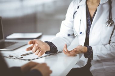 Bilinmeyen kadın-doktor, klinikteki dolapta birlikte otururken hastasıyla teşhisi hakkında konuşuyor. İşyerindeki doktor, yakın plan. Mükemmel bir tıbbi hizmet.