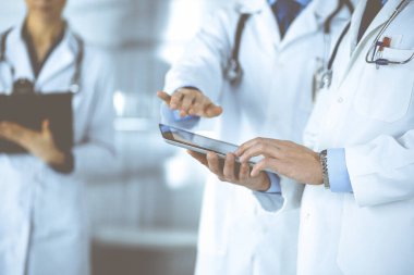 Bilinmeyen bir grup doktor hastane ofisinde dururken bazı tıbbi isim kayıtlarını kontrol etmek için bir bilgisayar tableti kullanıyor. Doktorlar hastaları muayene etmeye ve yardım etmeye hazır. Tıbbi yardım, sigorta