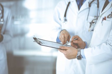 Bilinmeyen doktorlar, iki erkek ve bir kadın, hastane ofisinde dururken tıbbi muayene sonuçlarını tartışıyorlar. Doktorlar ilaç kayıtlarını doldurmak için pano kullanıyorlar. Mükemmel tıbbi servis.