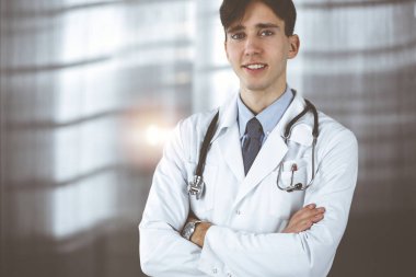 Klinikte kolları kavuşturulmuş gülümseyen adam-doktor. Hastanede genç ve zeki bir doktorla mükemmel bir tıbbi hizmet. Tıp konsepti