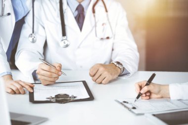 Bilinmeyen bir grup doktor masanın başında oturmuş güneşli hastane ofisinde hastalıkların tedavisini tartışıyorlar. Covid 2019