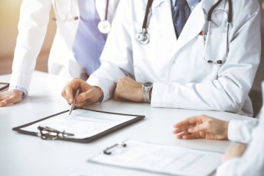 Bilinmeyen bir grup doktor masanın başında oturmuş güneşli hastane ofisinde hastalıkların tedavisini tartışıyorlar. Covid 2019
