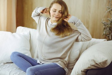 Mutlu esmer kadın ellerini başının arkasına koyuyor koltuğa yaslanıyor, Avrupalı kadın esniyor ve tembel haftasonunun keyfini çıkarıyor ya da sıcak oturma odasında tatilin tadını çıkarıyor.